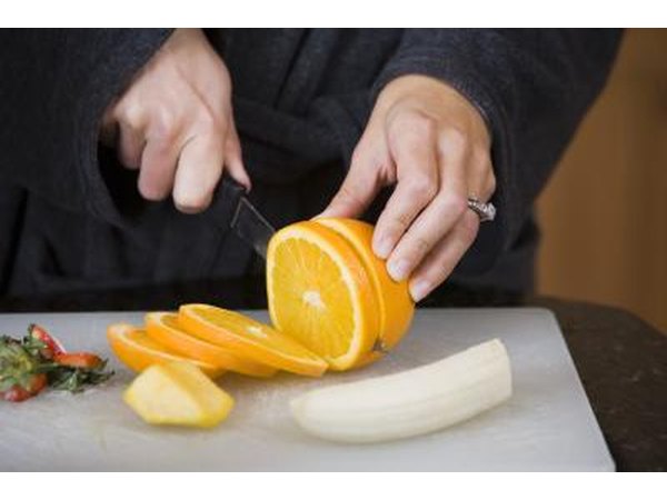 A woman slices an orange and banana.