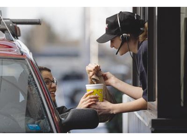 A fast-food employee hands a customer her order from a drive-thru window.