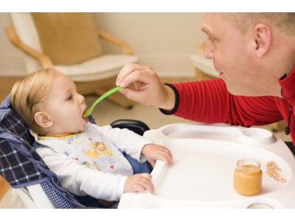 A man spoon feeds a baby in a highchair.