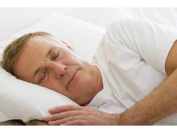 A middle aged man sleeps in a bed.