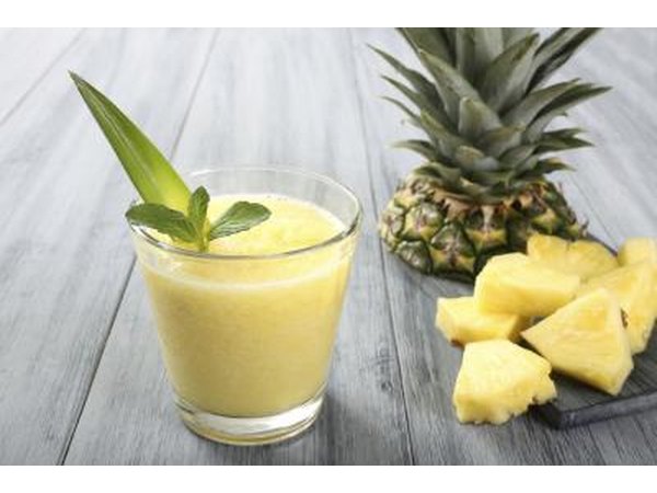 A glass of pineapple juice next to pineapple slices