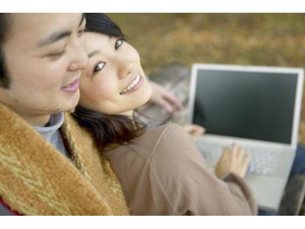 A man embraces a woman while she is looking at a computer.