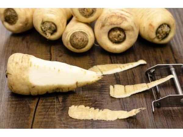 Parsnips with peeler on cutting board.