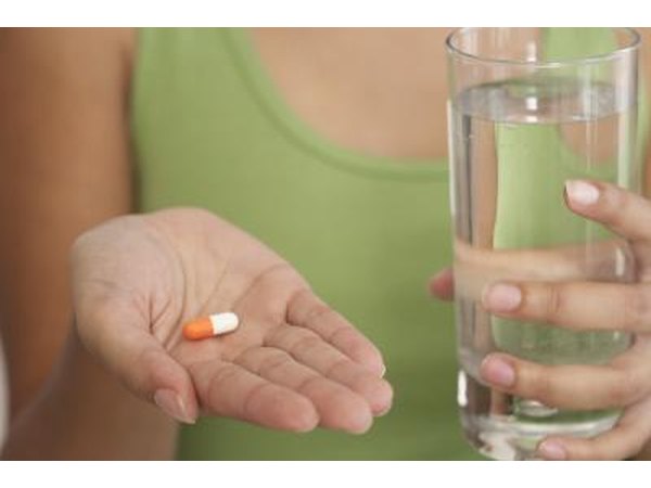 Woman holding capsule and glass of water.