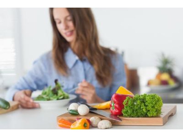 Woman eating salad with healthy vegetables in the foreground.