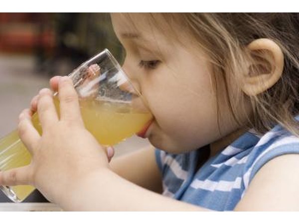 A little girl drinking a glass of apple juice at an outside table.
