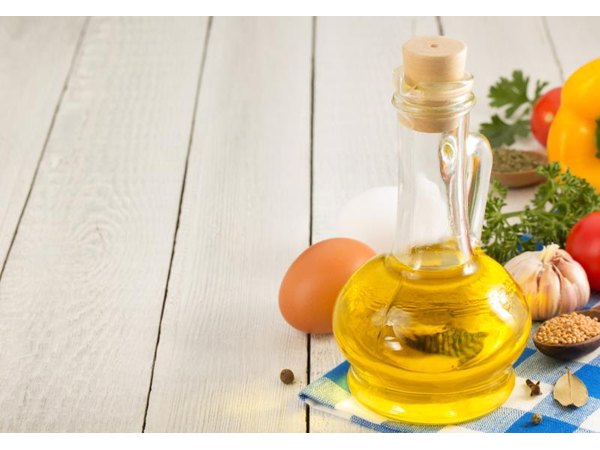Small bottle of corn oil on a table, next to some fresh food items.