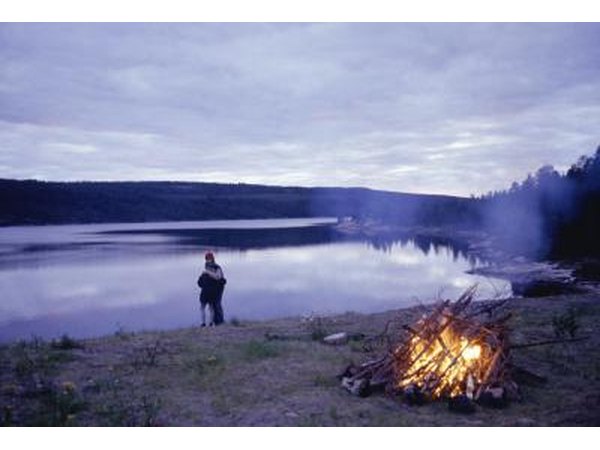 a couple standing on the shore with a campfire in the foreground.