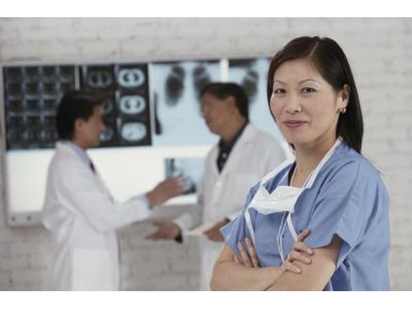 A female medical assistant standing in front of two doctors looking at X-ray prints.