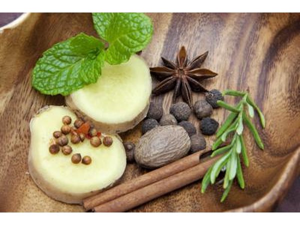 Fresh herbs and spices in a wooden bowl, including ginger, rosemary, cinnamon, nutmeg, mint, and anise.