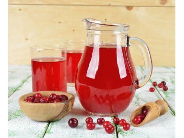 Pitcher and glasses filled with cranberry juice as well as a bowl of cranberries on a table