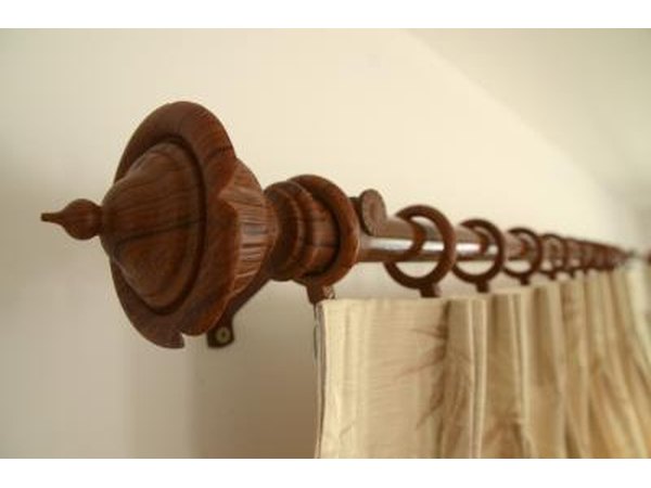 A close-up of pinch-pleat drapes hooked to a rings on a wooden bohemian style curtain rod.