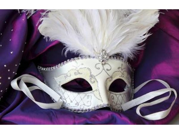 White masquerade Halloween mask lying on purple fabric.