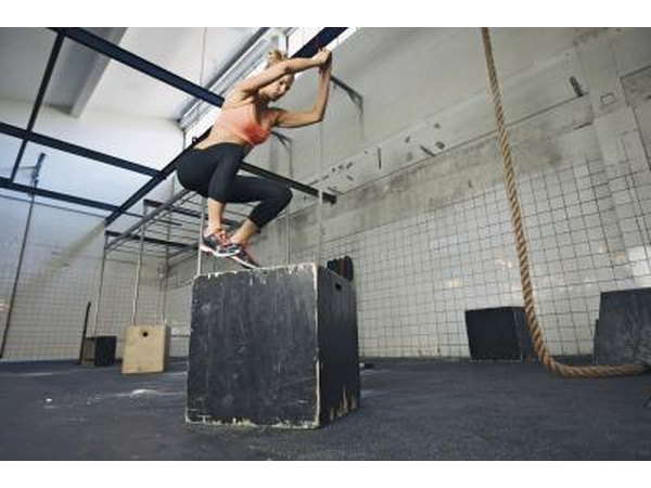 A woman performs plyometrics with a jump box.