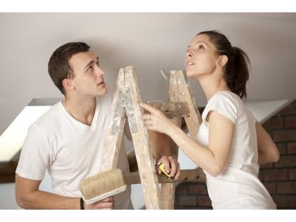 A couple on a ladder getting ready to paint a ceiling.