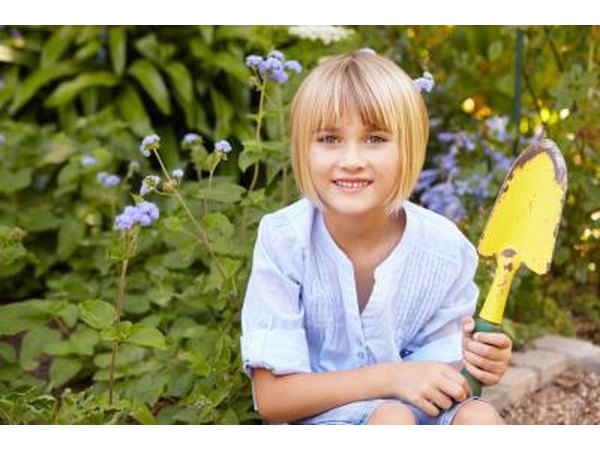 A girl holds a yellow spade in the garden.