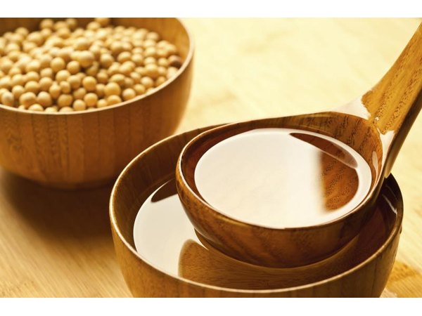 A small scoop of soybean oil, next to a bowl of soybeans.