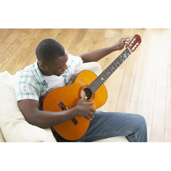 Monkey Business Images/Monkey Business/Getty Images Young Man Relaxing Sitting On Sofa Playing Acoustic Guitar