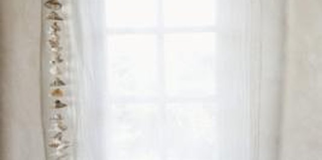 Jupiterimages/Goodshoot/Getty Images Hang a string of large shells to the side of a sheer curtain as a simple beach-inspired window treatment.