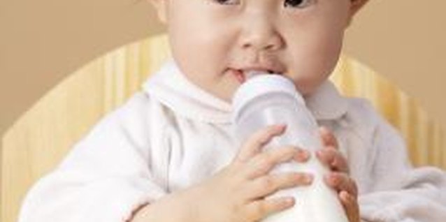 Sky View/Photodisc/Getty Images A baby begins to sit up with little support and hold her own bottle around 6 months.