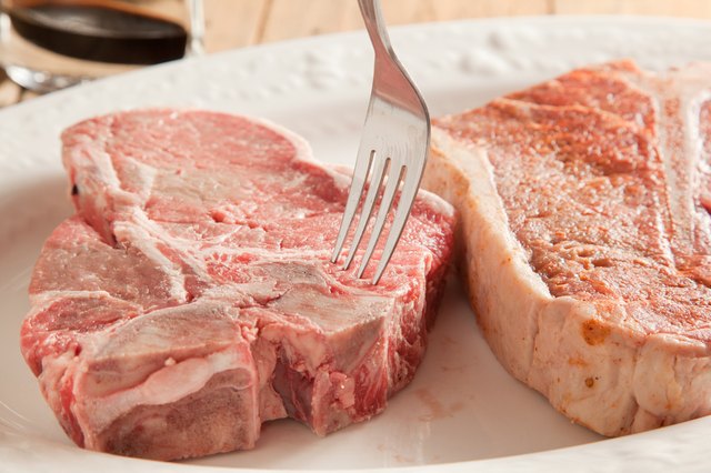 Raw t-bone steaks pierced with fork.