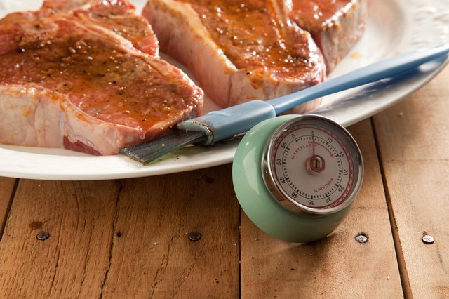 Kitchen timer next to raw t-bone steaks brushed with marinade.