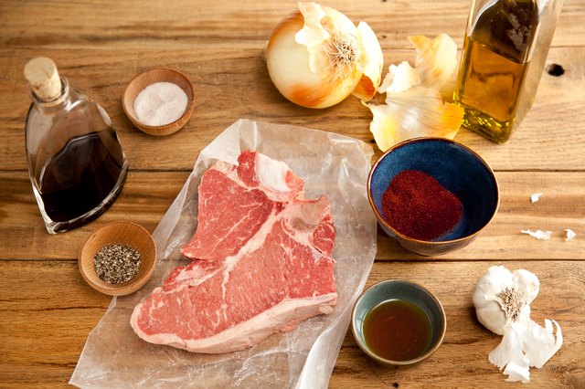 Raw t-bone steak with spices and olive oil on a cutting board.