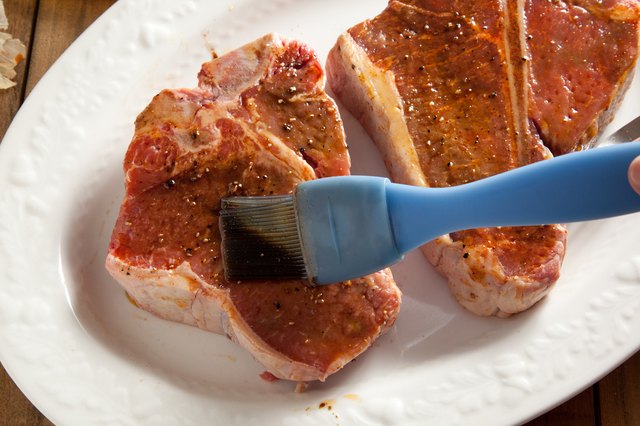 Brushing marinade on raw steaks.