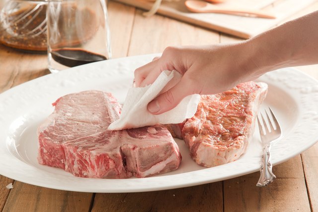Raw t-bone steaks blotted with paper towel.