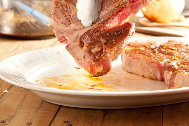 Raw t-bone steaks dripping over a plate.