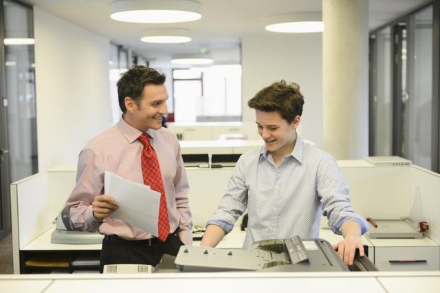 A young intern is working in a business office with a colleague.