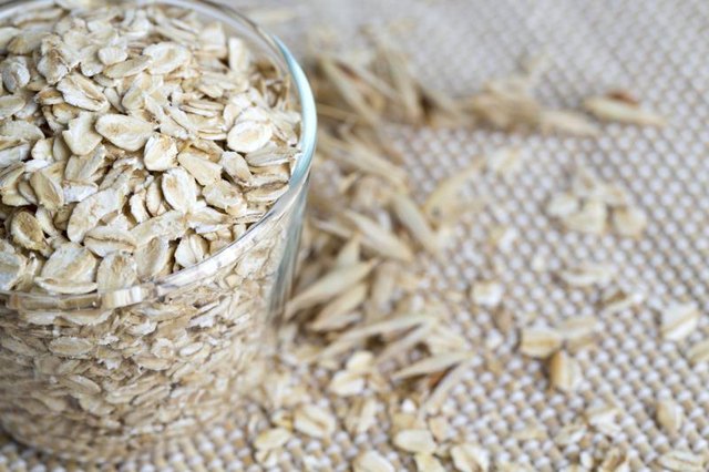 A glass cup filled with raw oat flakes.
