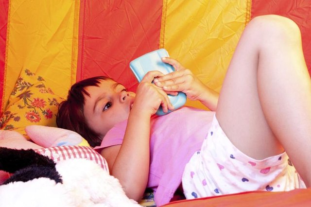 Young girl playing video games inside a tent.