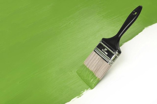 Paint brush spreading green paint on a white surface