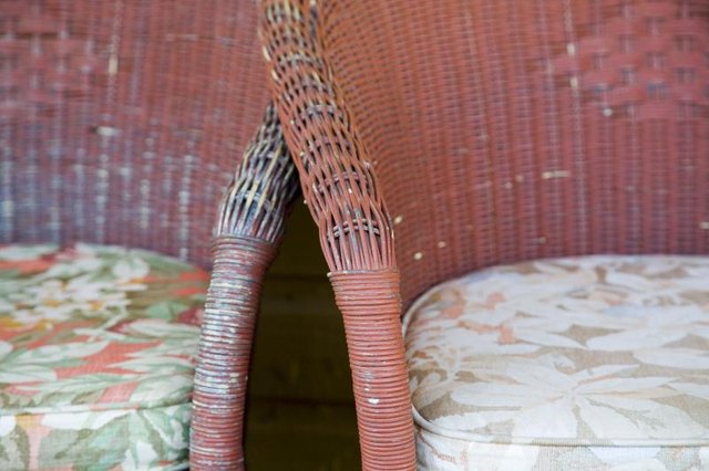 A close-up of faded paint on a pair of weathered wicker chairs.