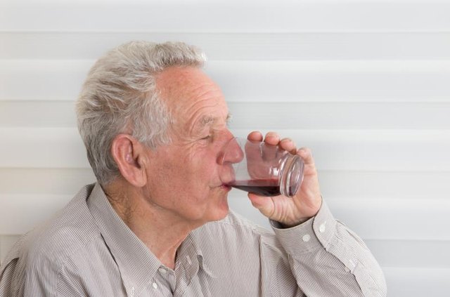 A man drinking a glass of cherry juice.