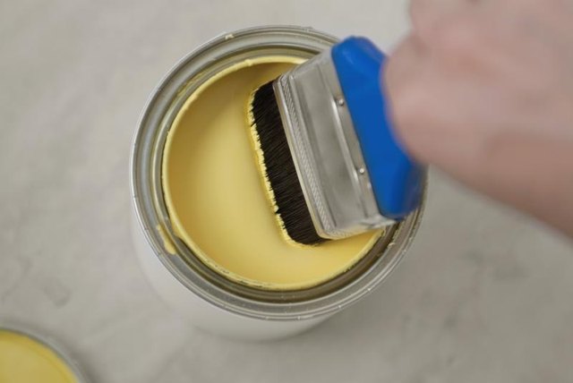 Close-up pale yellow paint in can with brush.