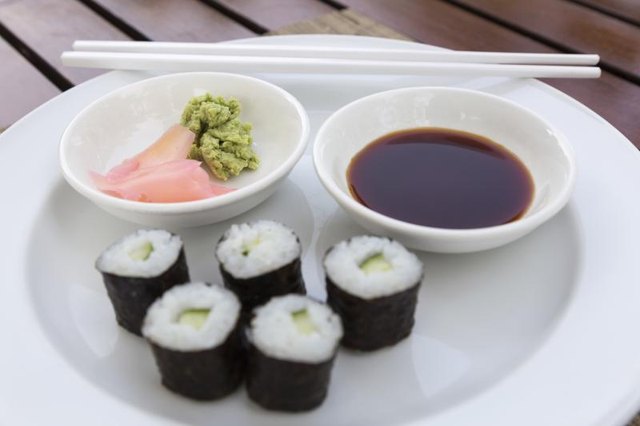 A sushi roll on a plate with soy sauce, wasabi and pickled ginger.