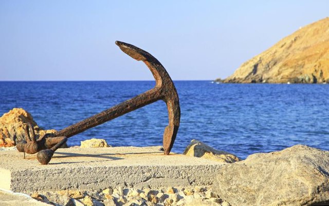An old anchor laying on rocks next to the ocean.