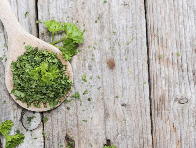 Wooden spoon filled with dried parsley.