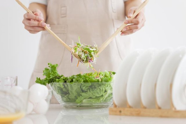 A woman is scooping salad into a bowl.
