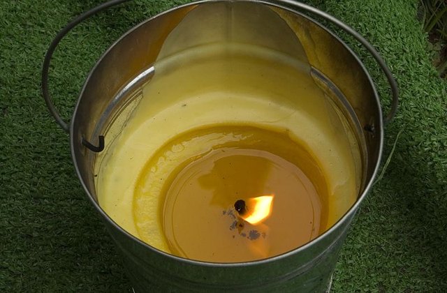 A lit citronella candle in a bucket burning outside.