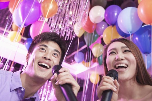 Friends singing karaoke together in decorated room.
