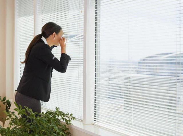 Woman looking out of her blinds from office window. Woman looking out of her blinds from office window.