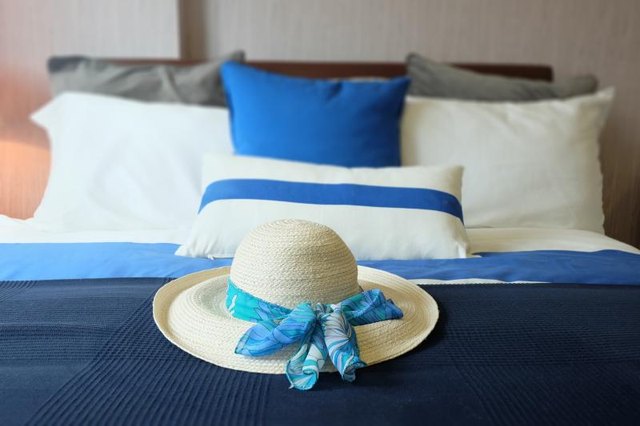 A close-up of a beach hat on a bed with various shades of blues. A close-up of a beach hat on a bed with various shades of blues.