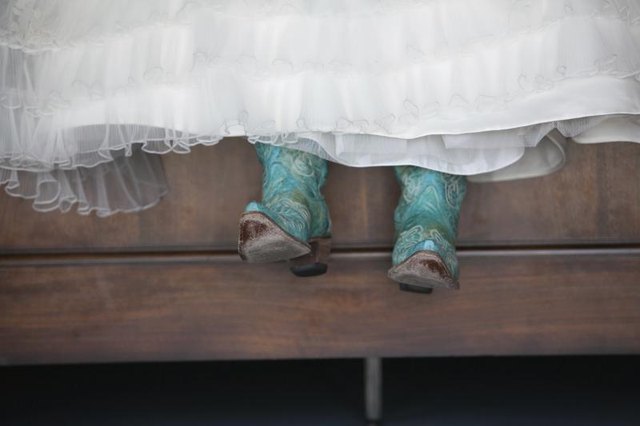 A bride's feet wearing cowboy boots below her wedding gown.