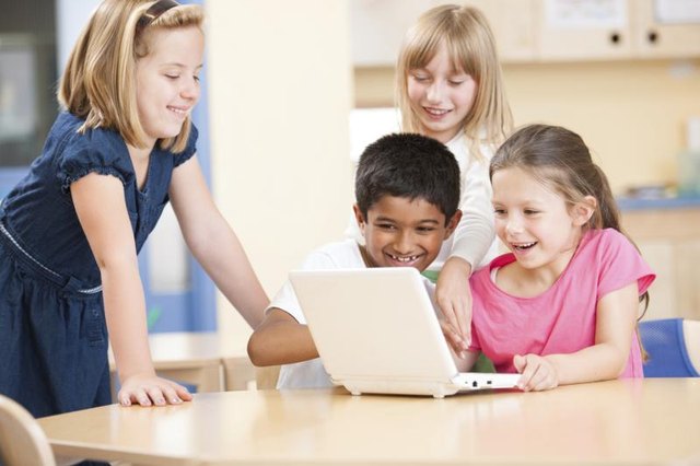 A group of first graders sit around a small learning laptop together A group of first graders sit around a small learning laptop together