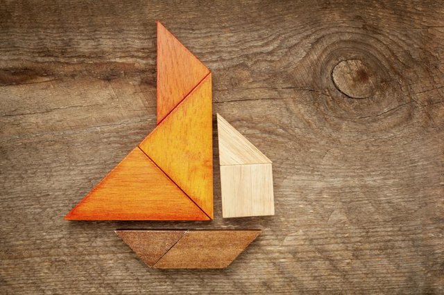 A tangram puzzle in the form of a sailboat, laying on a wooden table.
