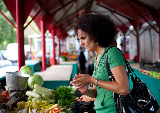 A woman buying vegetables at an outdoor farmer's market.