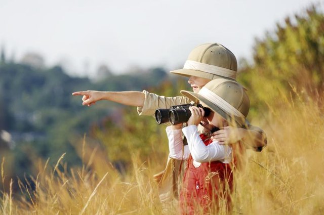 Boy and girl with safari hat using binoculars.